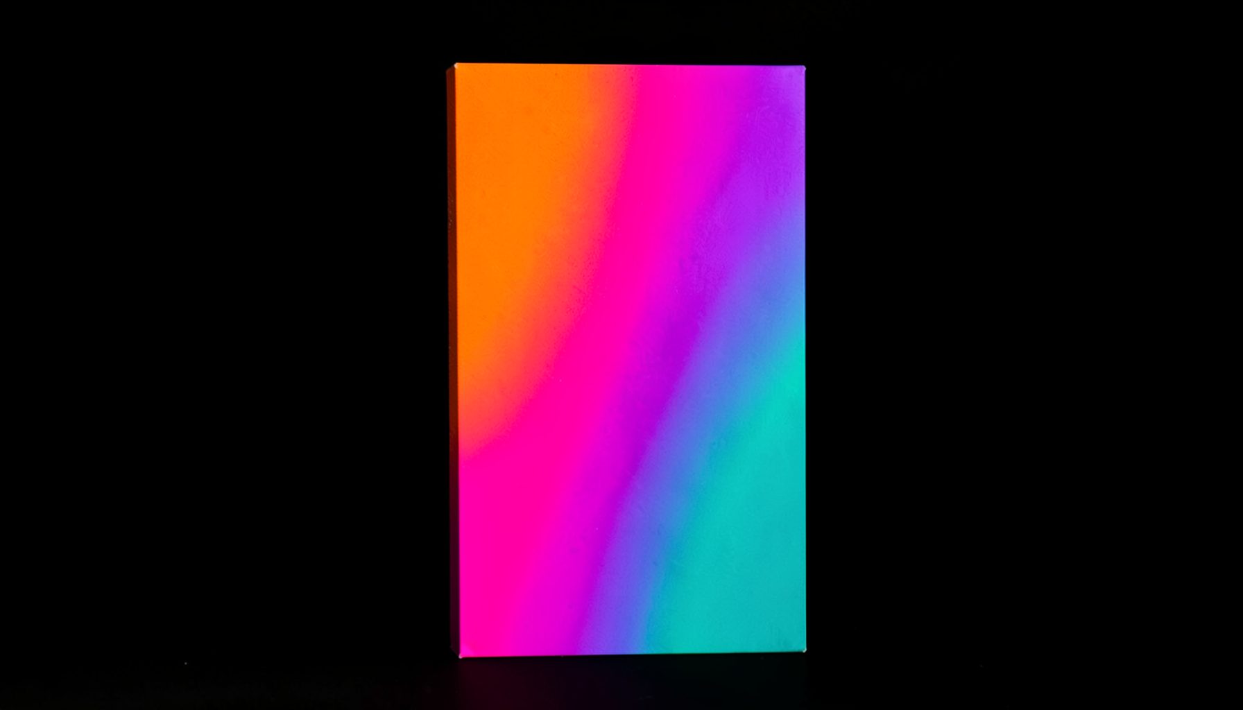 A bold vertical artwork block with a vivid multicolor gradient flowing from deep orange through hot pink into purple and teal, set against a near-black background.