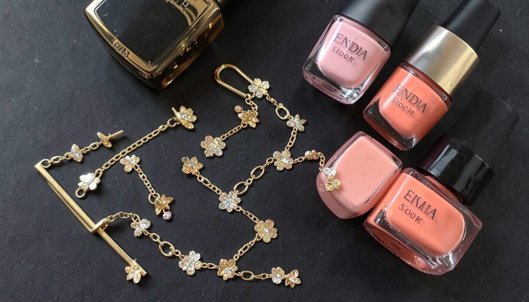 A stylish flat lay with Kendra Scott jewelry in warm gold and rose tones alongside glossy Essie nail polish bottles in soft pink shades.